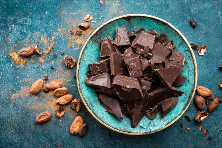 pieces-of-broken-dark-chocolate-in-a-turquoise-bowl-on-blue-stone-table-with-cocoa-beans-and-powder