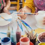 Woman coloring handmade dishes using brush to paint color